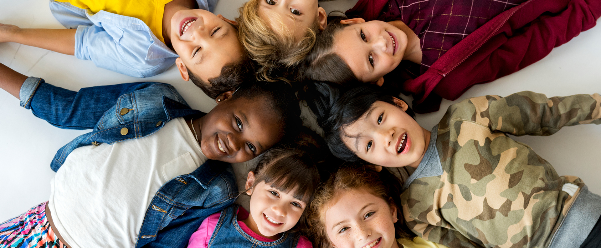 Group of multicultural children lying on the floor in a circle with heads meeting in the middle