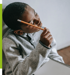 young black child sitting on a chair with a notepad holding a pencil to his head, thinking