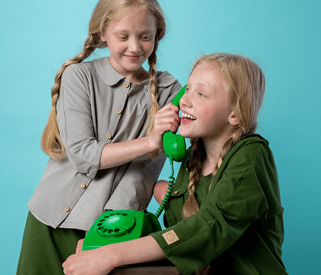 two girls with long blonde braided hair talking on a green rotarty phone