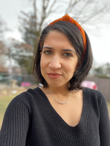portrait of a woman with a black v neck sweater and an orange headband