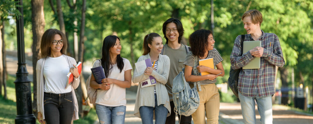 group of diverse cheerful students walking on a path holding school books